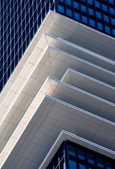 Three window cleaners suspended on ropes clean a modern glass building facade during the day.